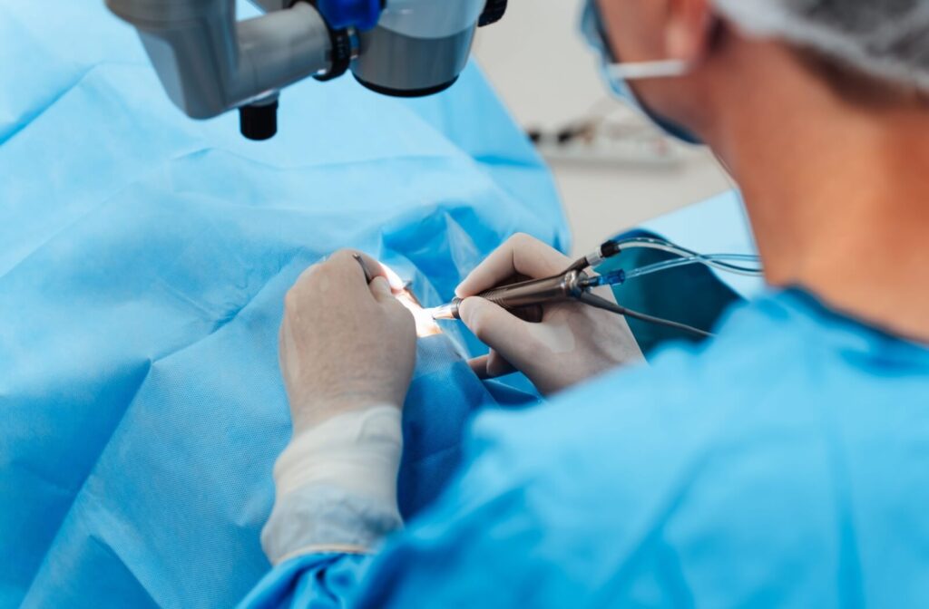 Surgeon using precision instruments under a surgical microscope, with blue sterile drapes.