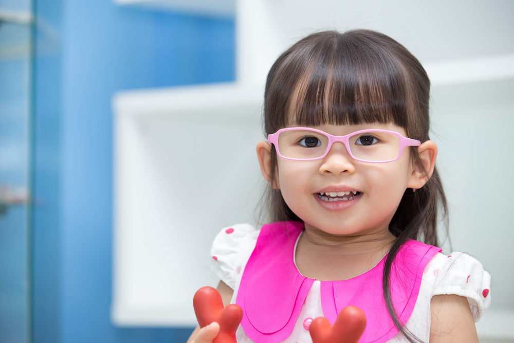 Smiling young girl with pink glasses and a bright pink outfit, indoors.